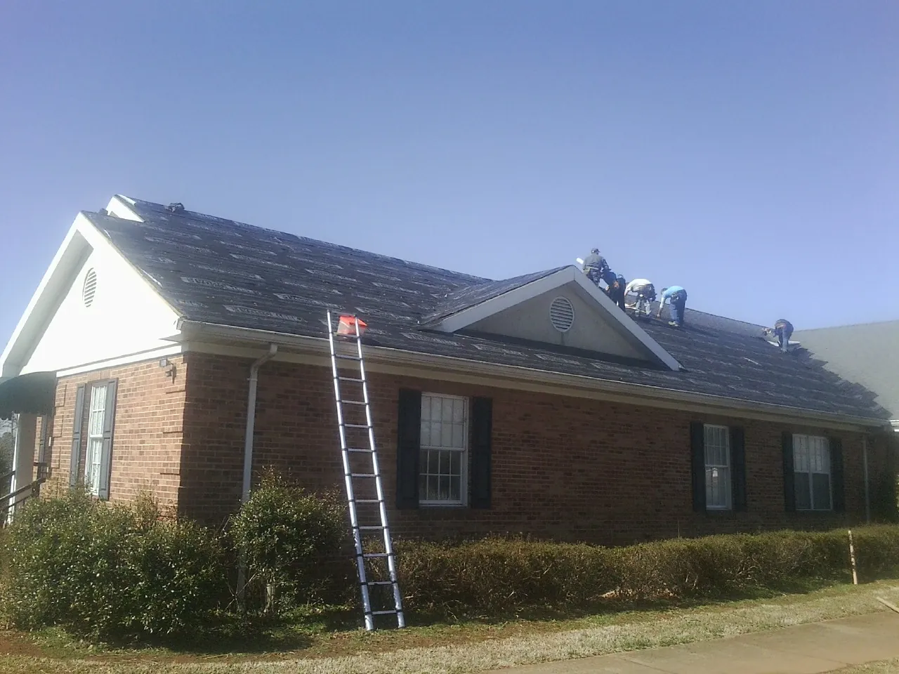 Crew tearing shingles off a brick ranch roof with a ladder set — Metal Roof Repair work by our crew in Dupo