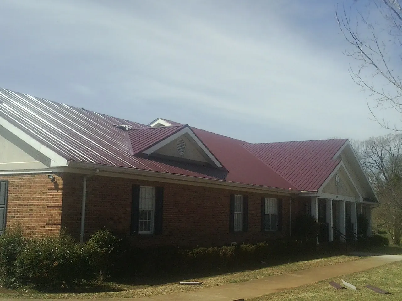 Red metal roof with gabled entries on a long brick building, from a Hail Damage Roof Repair job in Dupo
