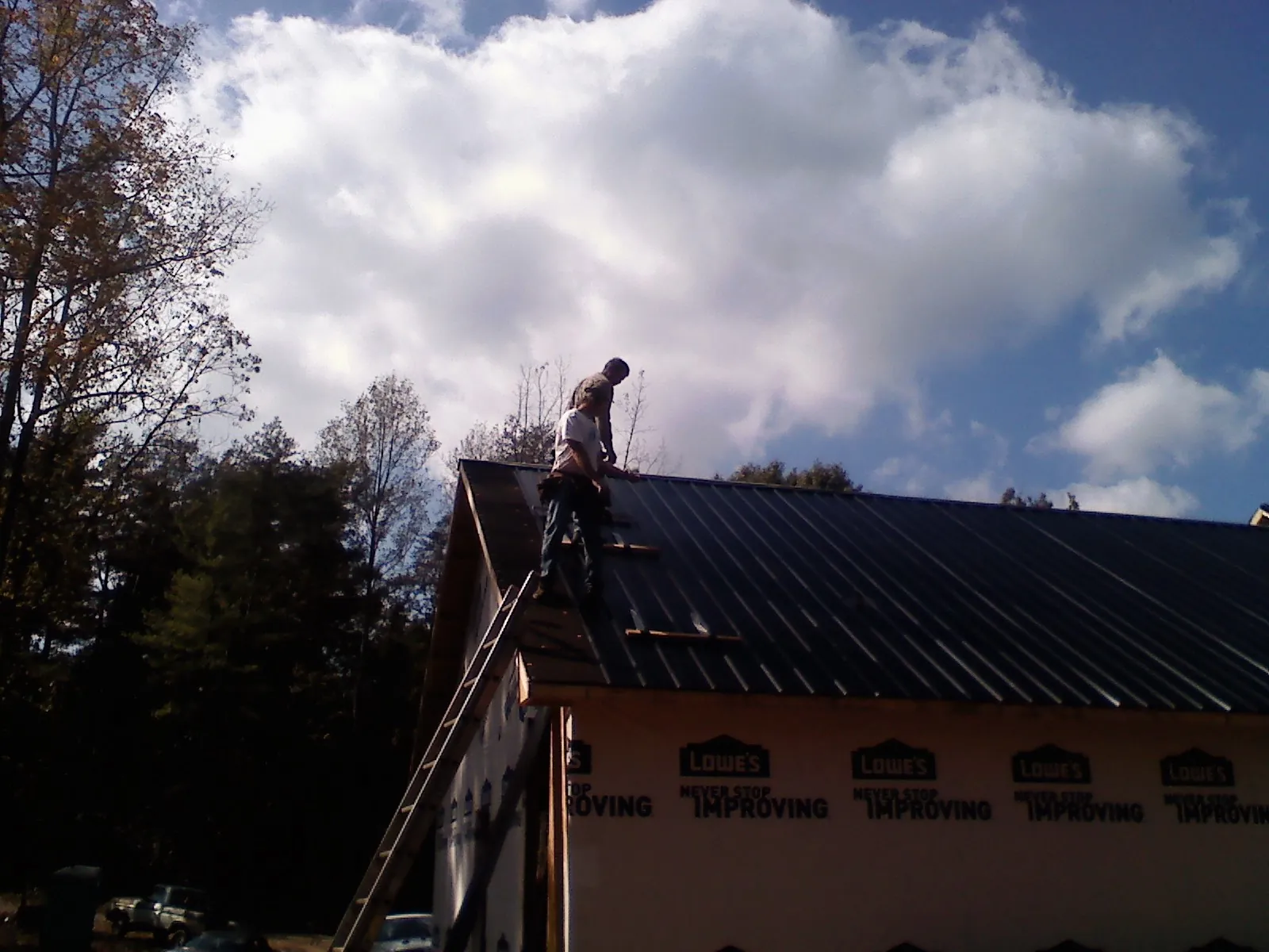Roofer fastening dark metal panels high against a cloudy sky, from a Roof Inspection job in Dupo