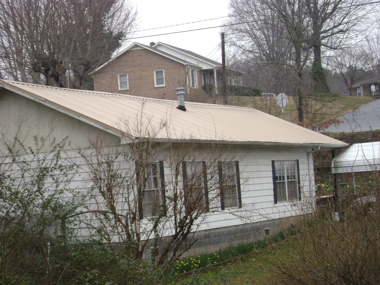 Tan metal roof on a white sided house set into a hillside — Commercial Roofing by Roofing Brothers in Dupo