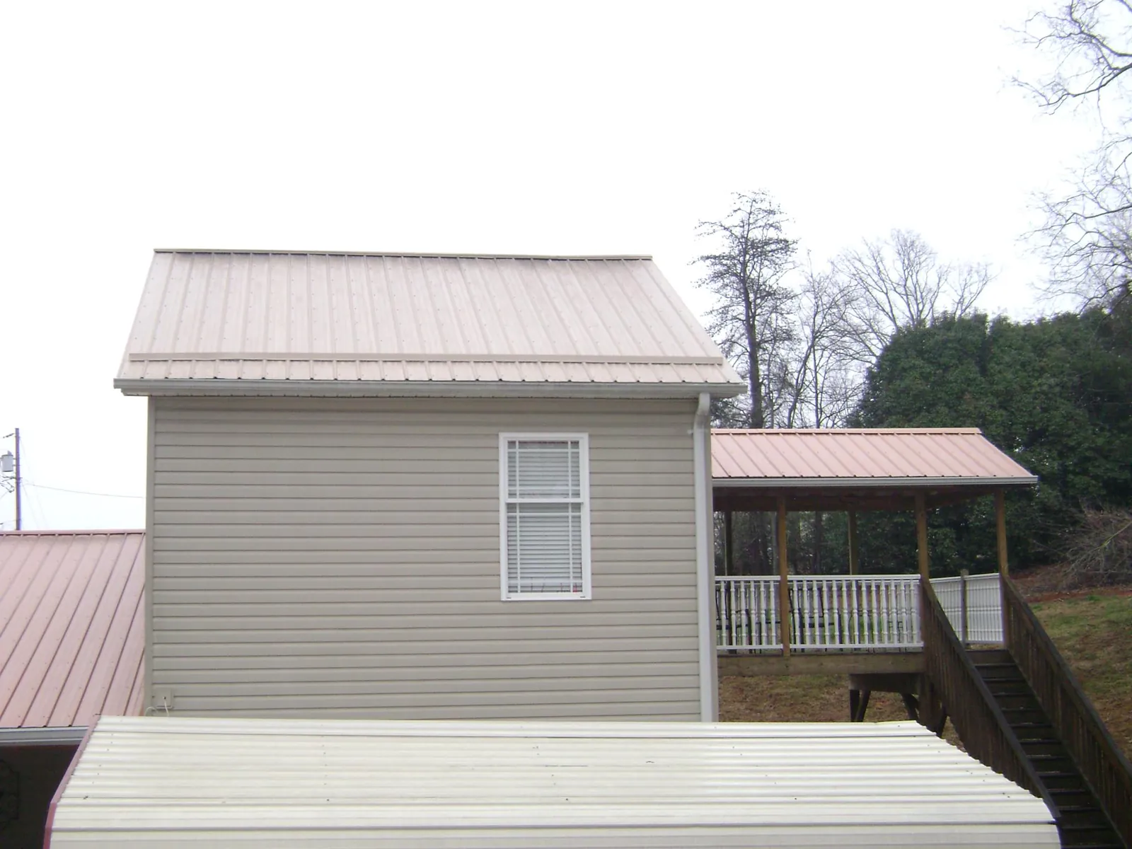 Tan metal roofs on a two story addition and attached porch, from a Roof Replacement job in Dupo